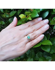 Heart-cut emerald engagement ring with diamond halo on a hand, set in 14K yellow gold.