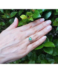 Heart-cut emerald engagement ring with diamond halo on a hand, set in 14K yellow gold.