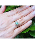 Heart-cut emerald engagement ring with diamond halo on a 14K yellow gold band, worn on a hand.