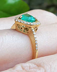 A 14k yellow gold ring with a natural emerald on a finger against a blurred natural background.