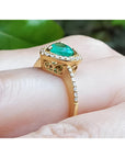 14K yellow gold ring with a heart-cut emerald surrounded by a diamond halo on a hand.