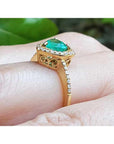 14K yellow gold ring with a heart-cut emerald surrounded by a diamond halo on a hand.