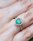 A heart cut emerald engagement ring halo diamonds 14k yellow gold. on a hand.