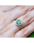Heart-cut emerald engagement ring with diamond halo on a 14K yellow gold band, worn on a finger.
