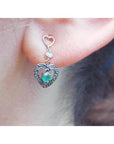 Emerald heart earring made of 14k gold worn on a woman's ear.
