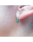 14K yellow gold heart earrings with brilliant cut Colombian emeralds, prong set, on an ear.