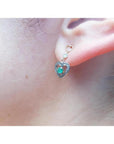 14K yellow gold heart earrings with brilliant cut Colombian emeralds, prong set, on an ear.