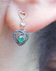 Emerald heart earring worn on a woman's ear, close-up view.