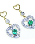 Pair of emerald heart earrings with round cut emeralds on a right position top view.