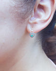 Woman's ear wearing a heart shaped earring with a round emerald.