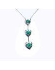 14K white gold journey pendant necklace with three heart-shaped settings, each holding a round green emerald.