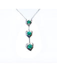 14K white gold journey pendant necklace with three heart-shaped settings, each holding a round green emerald.