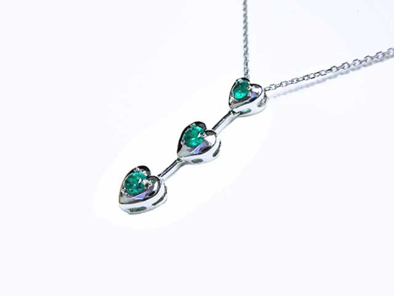 White gold necklace with natural emeralds heart-shaped stones on a white background