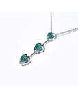 14K white gold heart journey pendant necklace with three round Colombian emeralds.