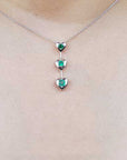White gold necklace with heart-shaped emerald pendants on a person wearing a light-colored top.
