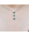 White gold necklace with heart-shaped emerald pendants on a person wearing a light-colored top.