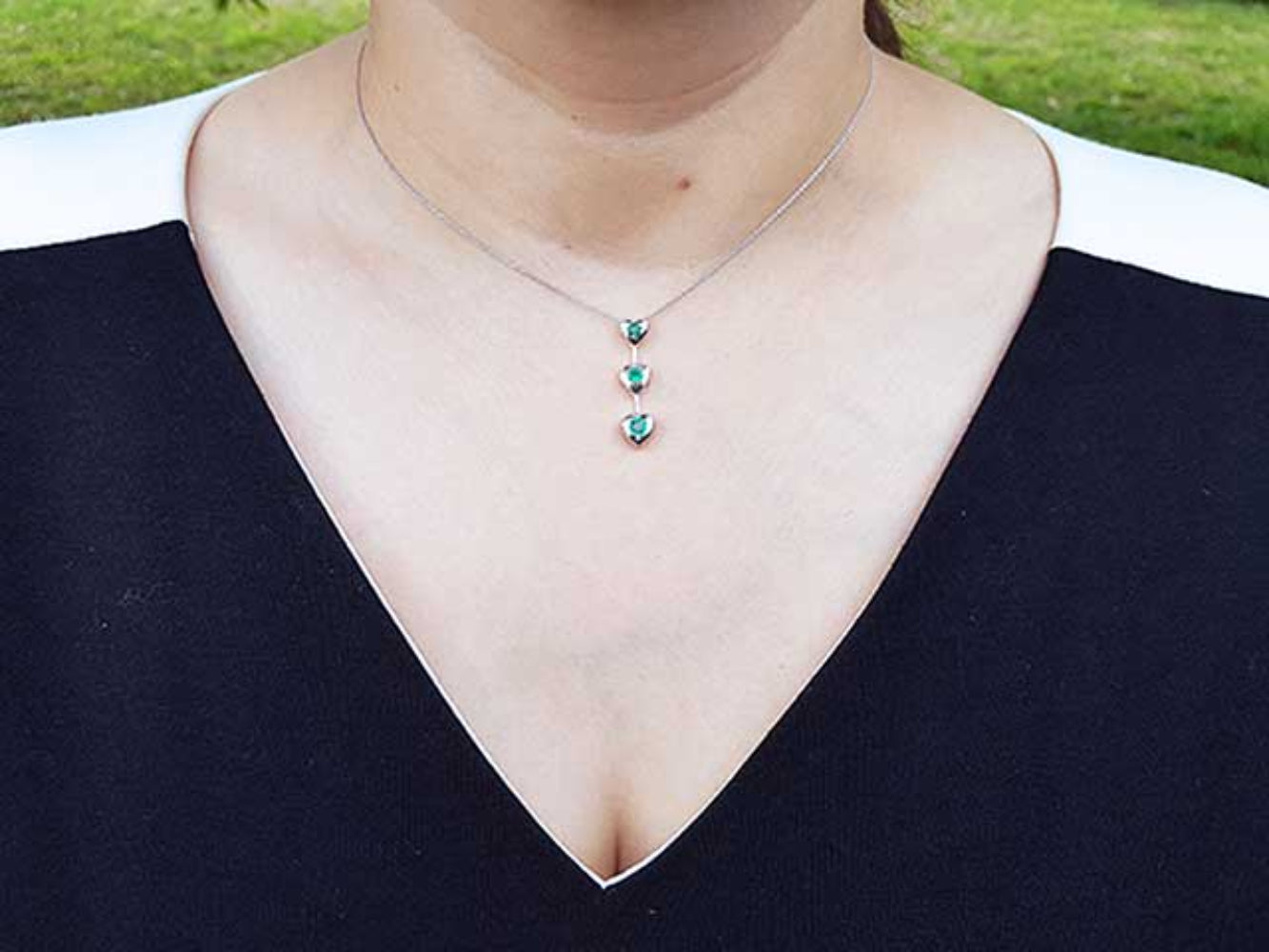 Necklace with three round cut natural emeralds worn by a person in a black top.