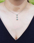 Necklace with three round cut natural emeralds worn by a person in a black top.