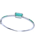 This topside profile view of a white gold emerald bangle bracelet displays the main central stone and side design.