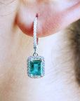 Close-up of a diamond emerald drop earring worn on an ear.