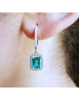 Close-up of a diamond emerald drop earring worn on an ear.