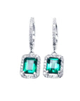 Pair of emerald hoop earrings with diamond accents on a front position, top view.