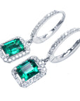 A pair of Muzo Colombian emerald dangle earrings, with halo diamond, left side profile and top visibles.