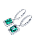 A pair of Muzo Colombian emerald dangle earrings, with halo diamond, left side profile and top visibles.