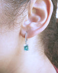 Close-up of an ear wearing a natural emerald hoop earring with a blurred background.