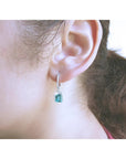 Emerald dangle hoop earrings with diamonds in 14k white gold on an ear.