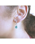 Emerald dangle hoop earrings with diamonds in 14k white gold on an ear.