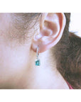 Emerald dangle hoop earrings with diamonds in 14k white gold on an ear.
