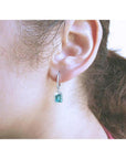Emerald dangle hoop earrings with diamonds in 14k white gold on an ear.
