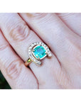14K yellow gold horseshoe ring with a cushion-cut emerald and diamond halo, worn on a hand.