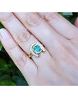 14K yellow gold horseshoe ring with cushion-cut emerald and diamond accents on a woman's hand.