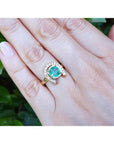 14K yellow gold horseshoe ring with cushion-cut emerald and diamond accents on a woman's hand.