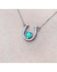 14K white gold horseshoe necklace with a prong-set oval emerald and natural diamonds.