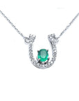 14K white gold horseshoe necklace with a central oval emerald and diamond accents.