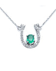 14K white gold horseshoe necklace with a central oval emerald and diamond accents.