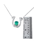 14K white gold horseshoe necklace with oval emerald and diamond accents, shown with ruler for size.