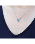 White gold oval emerald horseshoe necklace with diamonds, worn on a person.