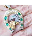 White and yellow gold pendant with horse design and emerald stones and diamonds held on a hand.