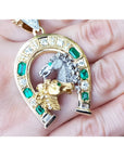 18K yellow gold horseshoe pendant with emeralds, diamonds, and two horse heads.