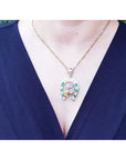 Necklace with a horseshoe emerald and diamond pendant on a person wearing a blue top.