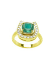 This yellow gold ring showcases a cushion-cut emerald set at the center of a horseshoe-shaped diamond design.