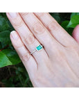 Hand wearing a 14K white gold ring with a bezel-set emerald and prong-set accent diamonds.