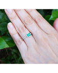 Hand wearing a 14K white gold ring with a bezel-set emerald and prong-set accent diamonds.