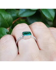 0.73 ct bezel set emerald ring with accent diamonds on a 14K white gold band, worn on a finger.