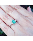 1.47 ct emerald cut emerald engagement ring with diamond halo in 14K white gold on a hand.