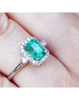 1.47 ct emerald cut emerald ring with diamond halo in 14K white gold on a finger.